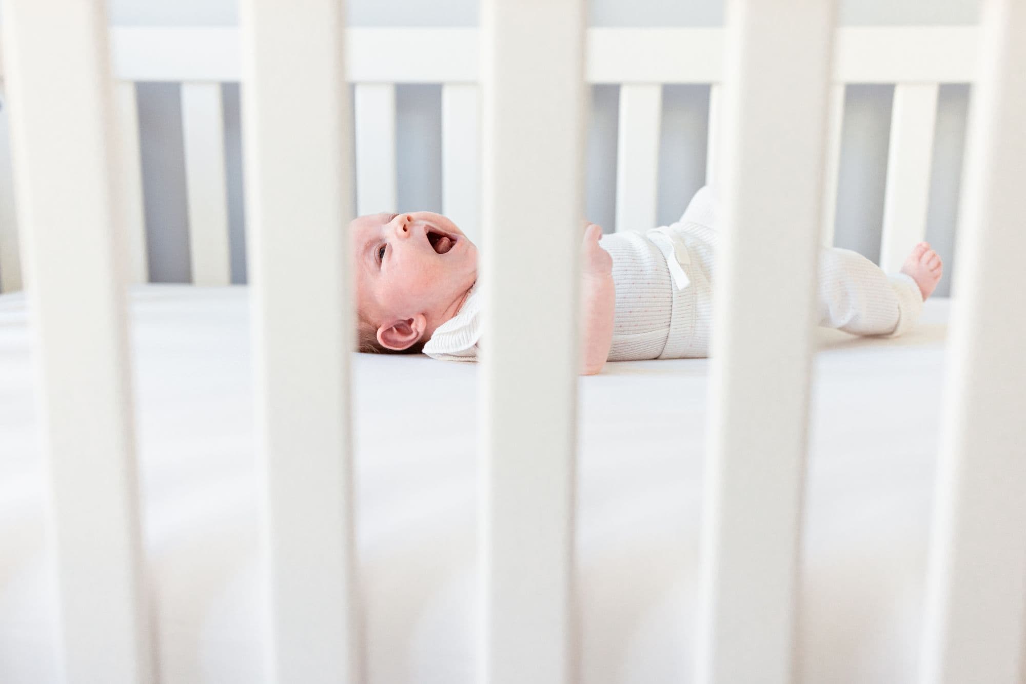 Baby crying in white crib captured by San Francisco newborn photographer