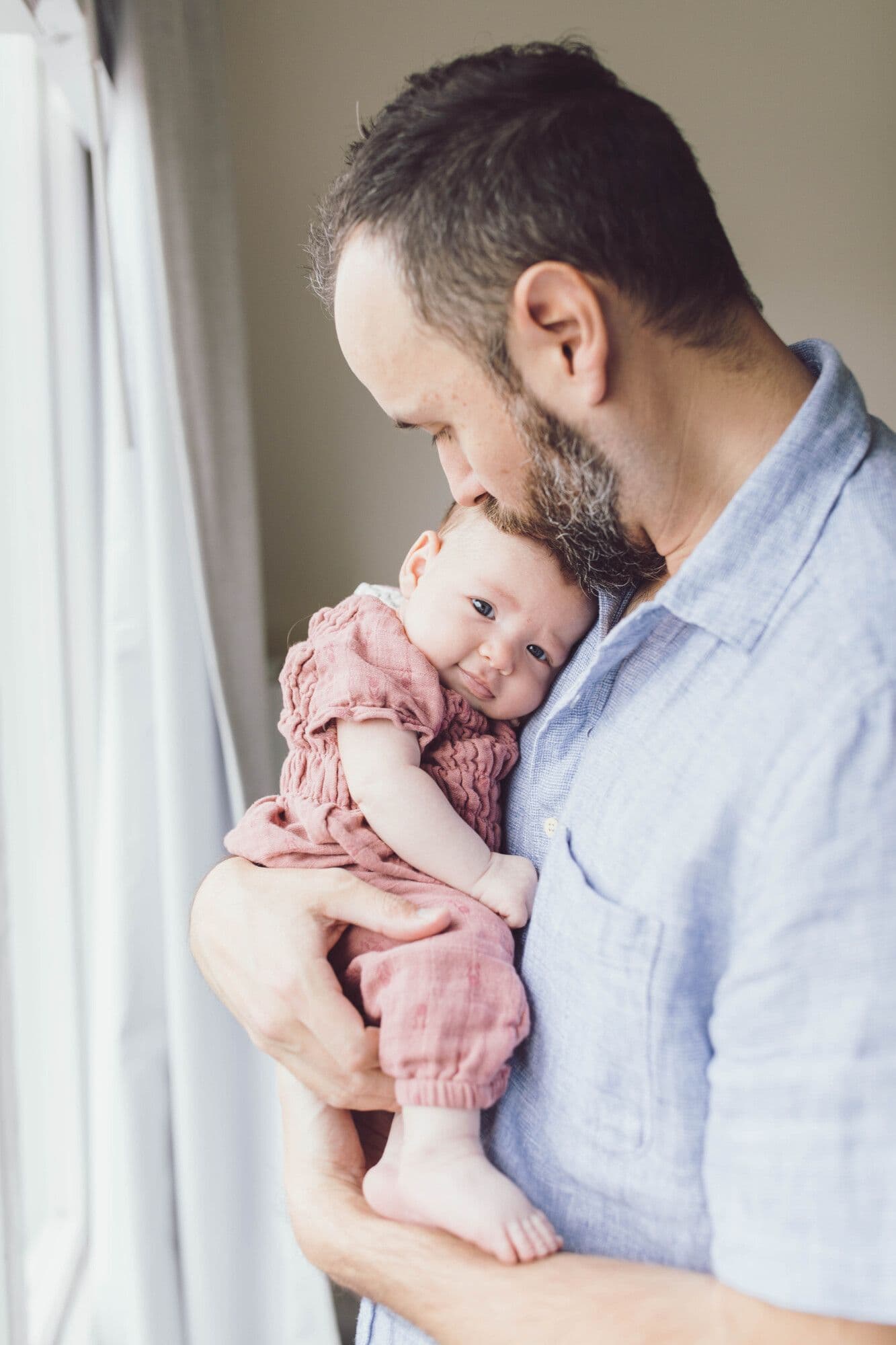 Father tenderly holding newborn baby in pink outfit during photography session